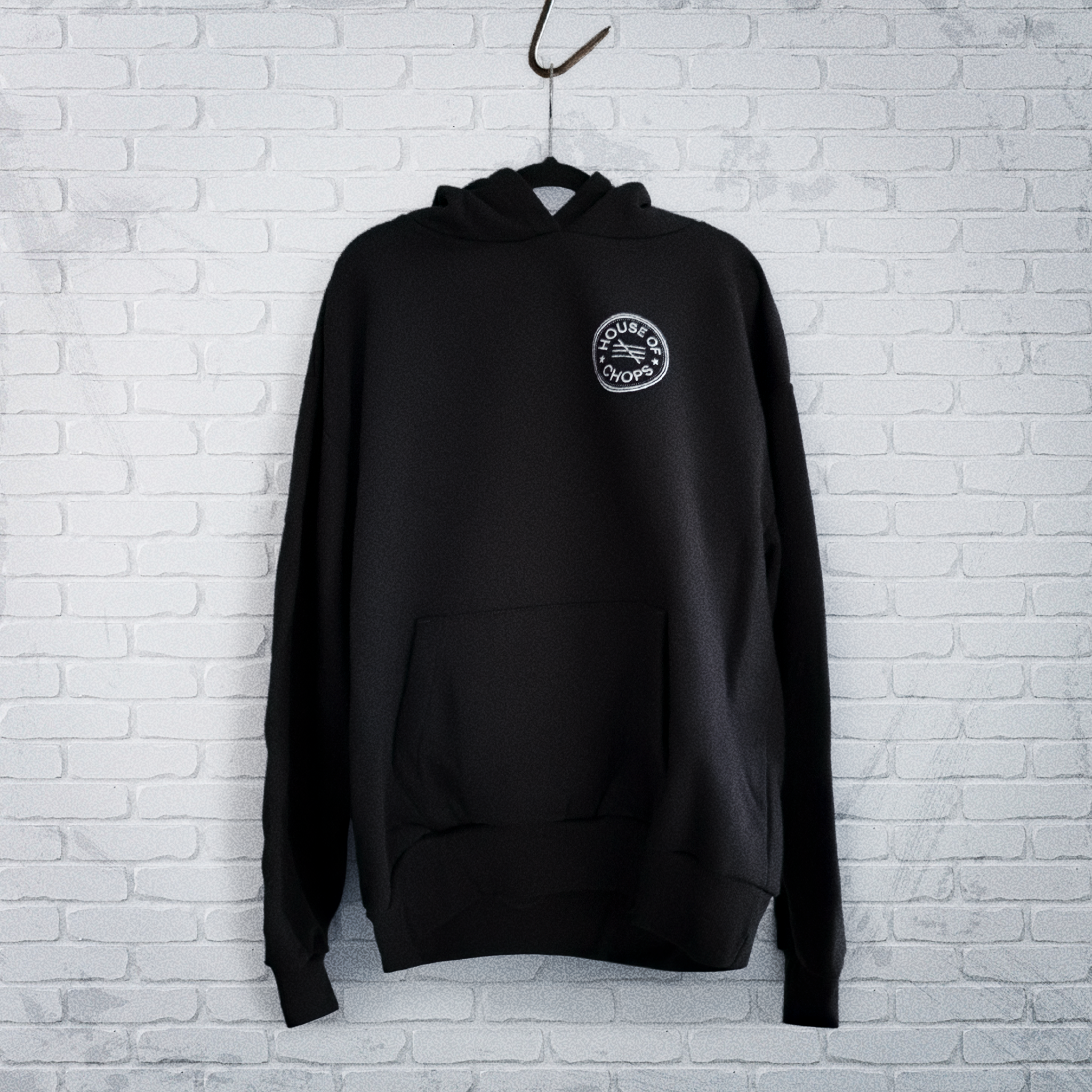 Cut 001 black hoodie front displayed on hanger showing natural drape and heavyweight fabric construction - against a white wall.